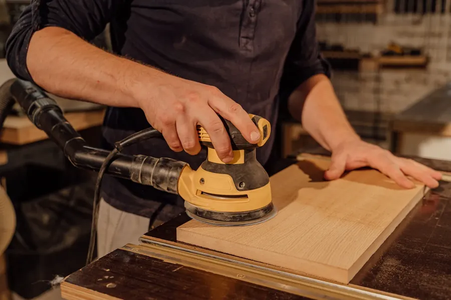 Person sanding a timber panel in a workshop. Representative stock photography, not a deck project.